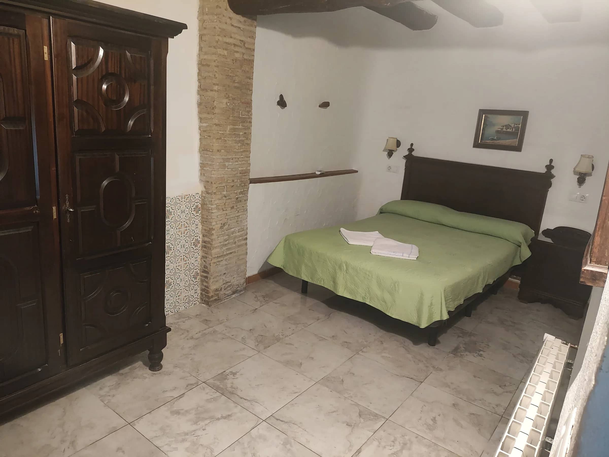 Dormitorio de matrimonio en la planta baja con armario antiguo y pilar de ladrillo visto