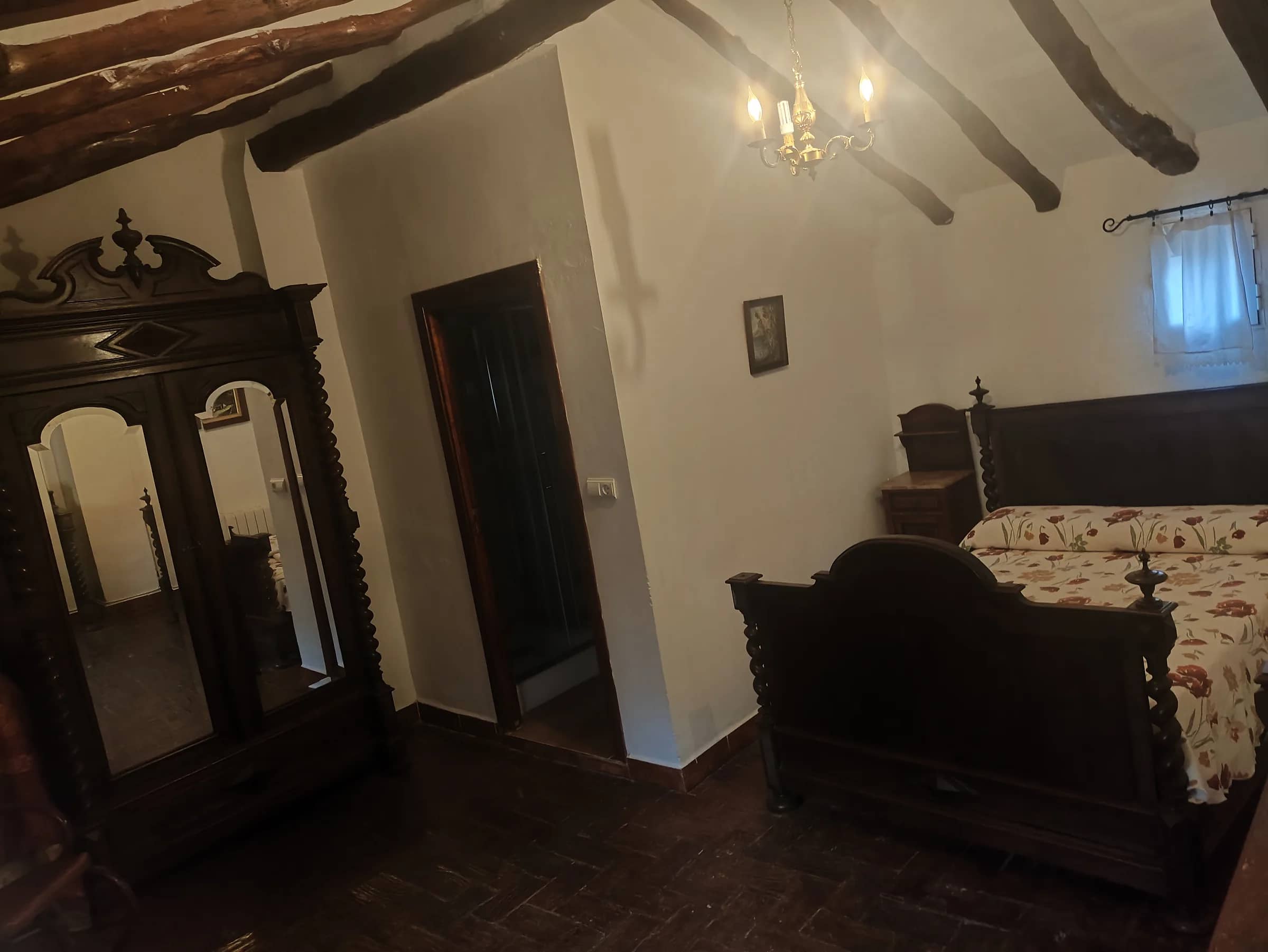 Dormitorio de matrimonio con cabecero tallado, armario de luna y lámpara de araña