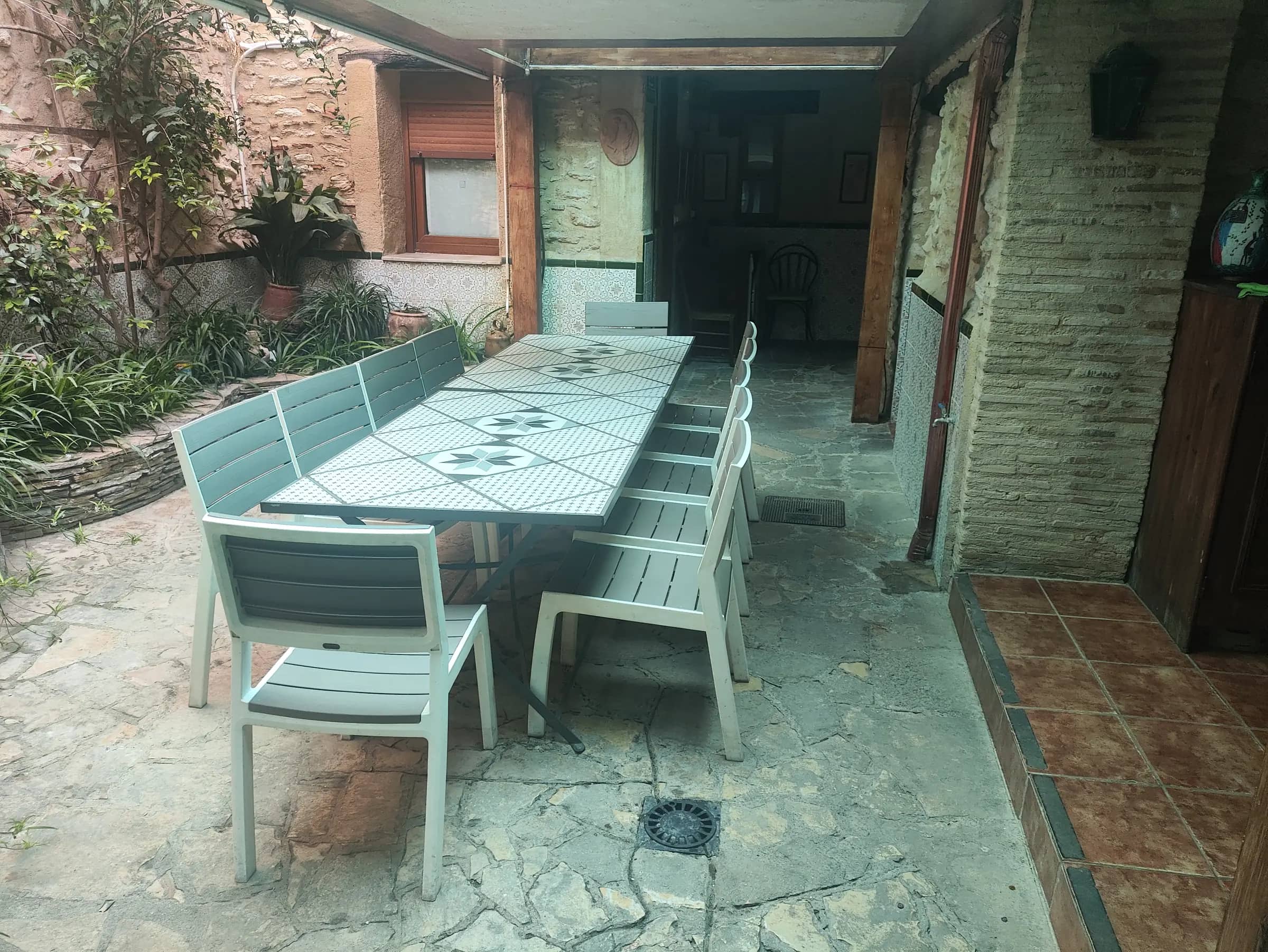 Mesa larga del patio con sillas para todo el grupo y plantas en los muros de piedra
