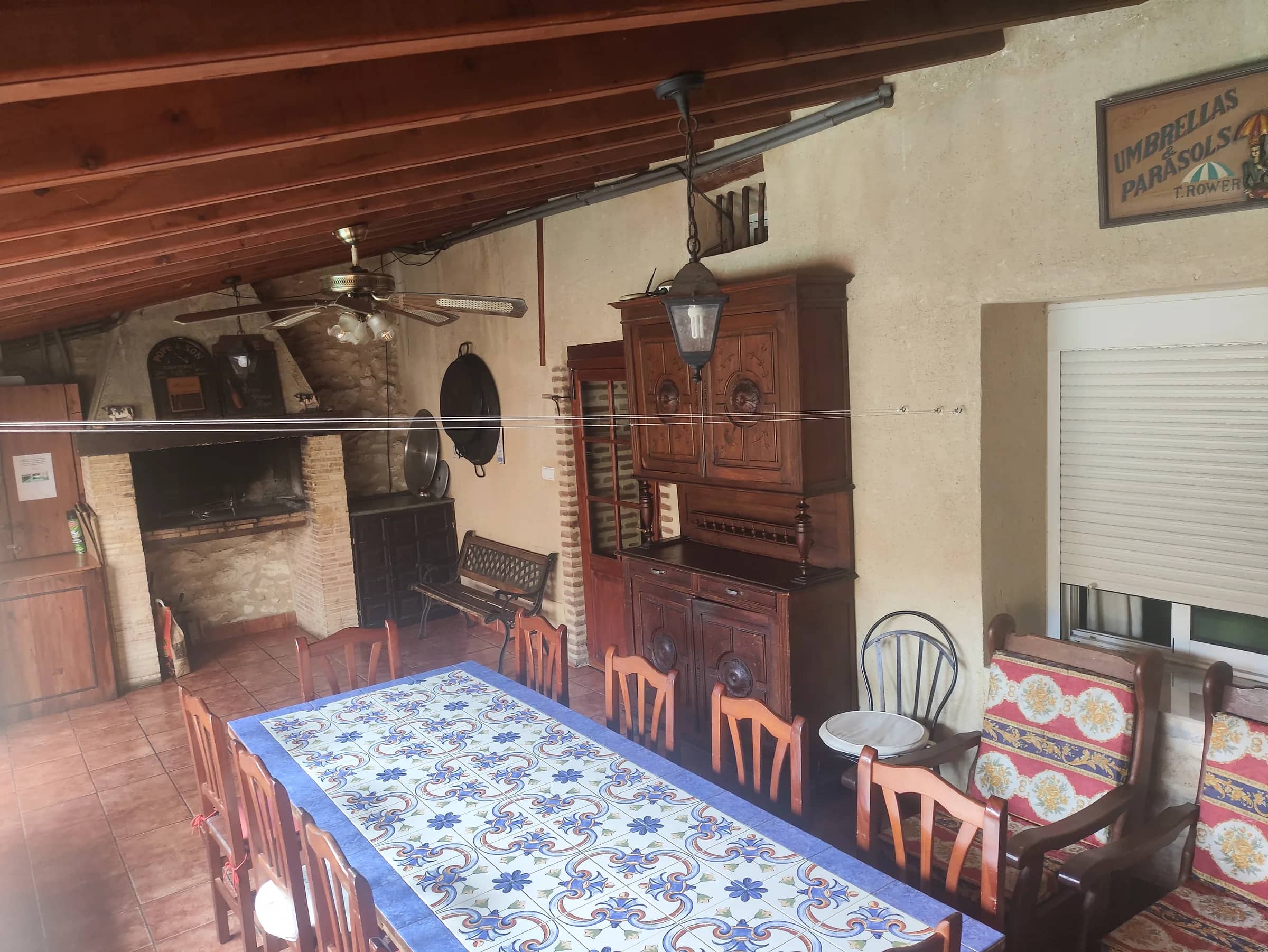 Comedor de verano cubierto con vigas de madera, ventilador y barbacoa de obra